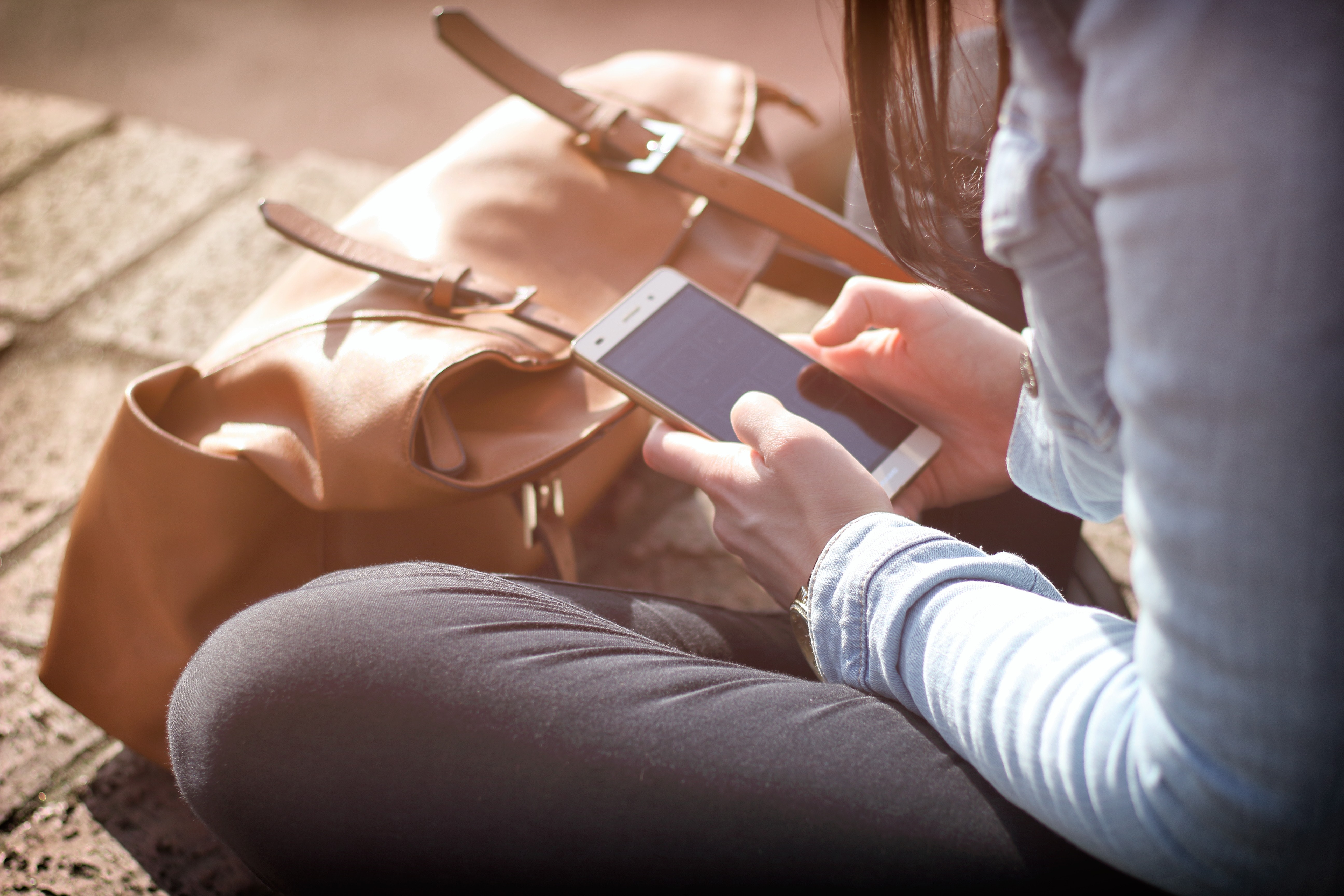 Person sitting next to their bag using a smartphone